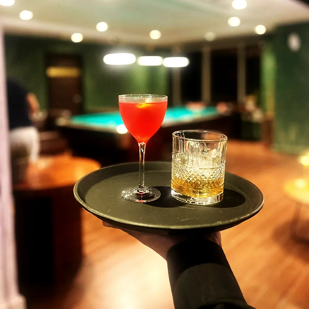Two cocktails on a tray with the billiards table behind