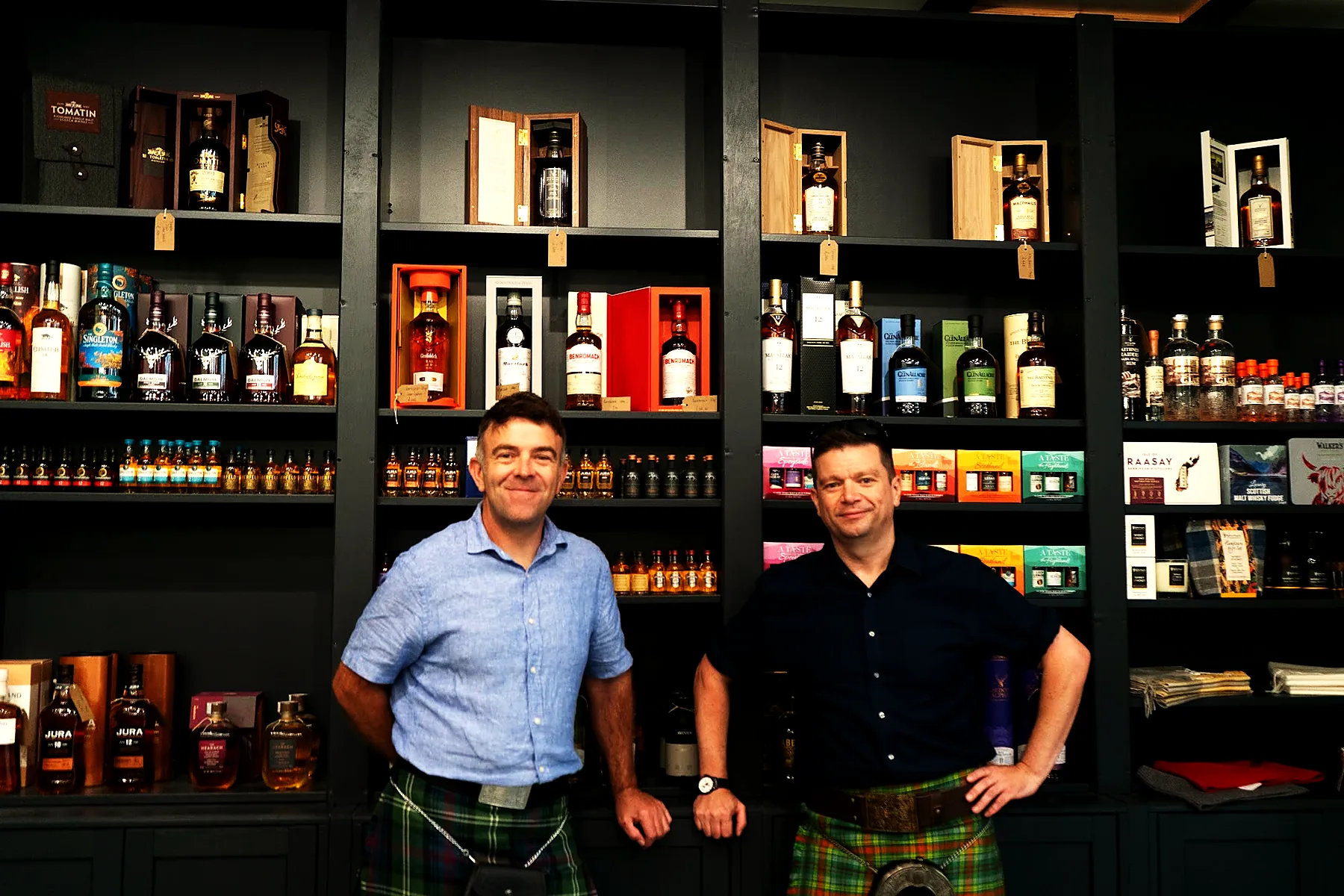 Two of the Wild Woven team in kilts in front of the whisky wall