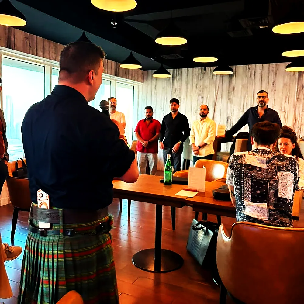 A host in a kilt addressing guests at a Wild Woven event