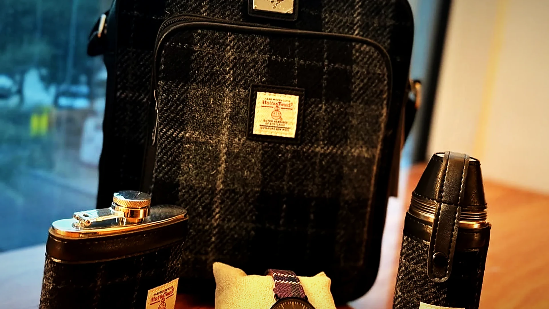 A Harris Tweed bag, hip flasks and a watch arranged on timber