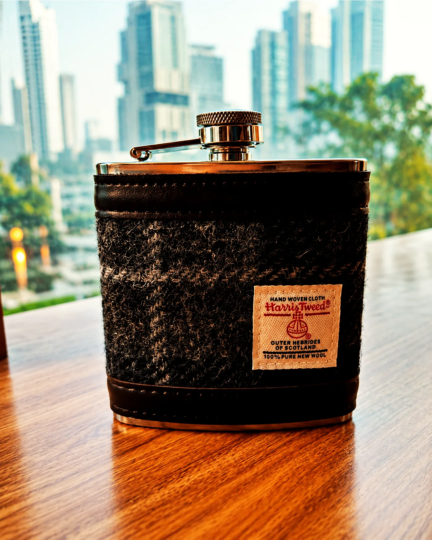 A Harris Tweed hip flask on a timber table with the Dubai skyline behind