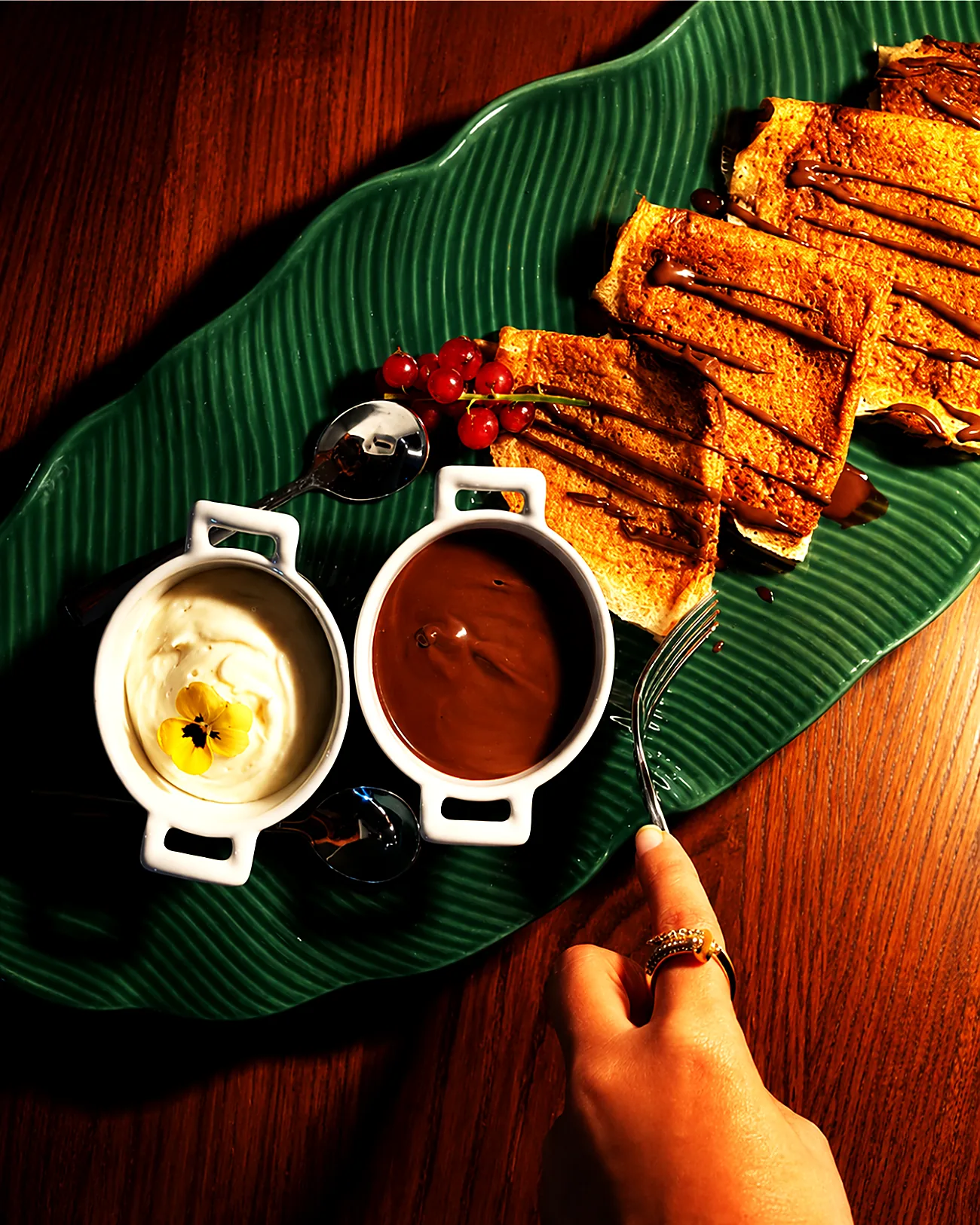 A hand reaching for barley crepes on a green serving board