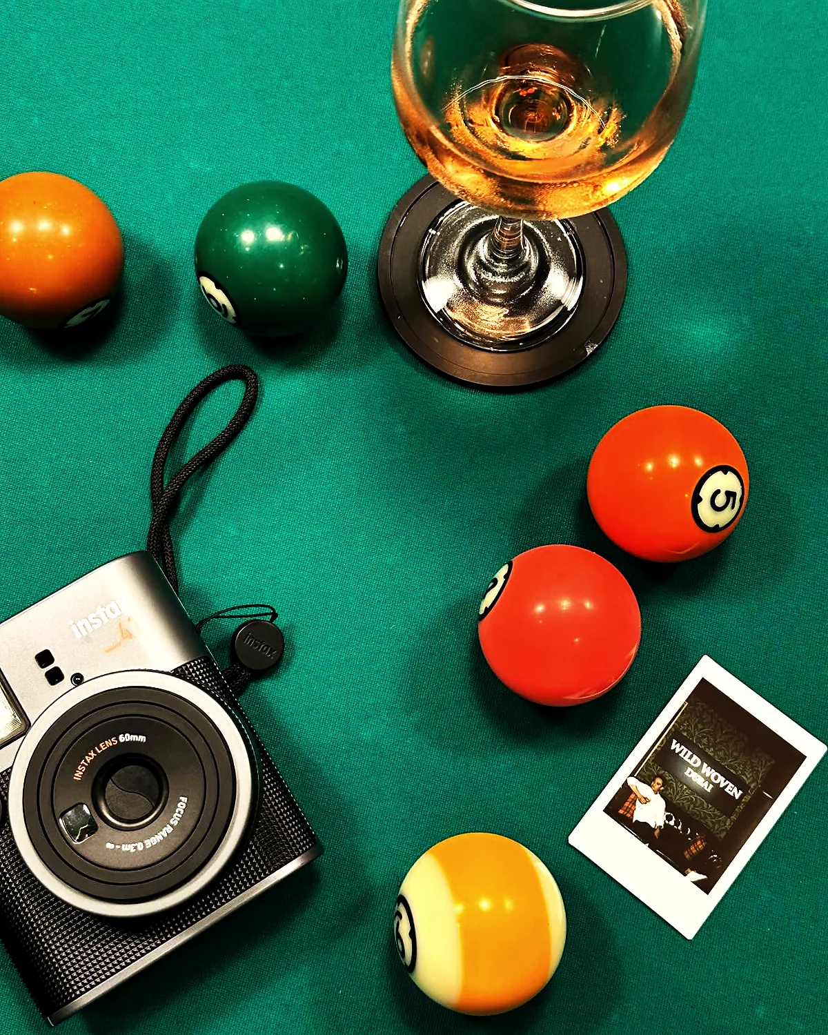 A dram, billiard balls and a polaroid arranged on the green baize